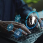 Digital cyber security concept. Person working on laptop with firewall, encryption and shield icons, hacking prevention, data privacy and IT security management.